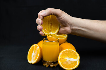 Fresh squeezed orange juice on a black background. A man squeezes orange juice into a glass. Orange juice with oranges on a black background. © Регина Ерофеева