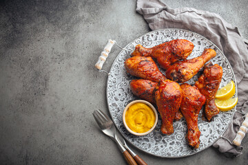 Traditional Indian dish Tandoori chicken legs served with exotic yellow sauce and lemon wedges on rustic aluminum plate on grey concrete background from above with space for text