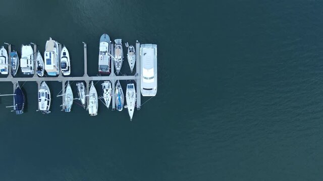 A static high drone view looking down at multiple boats docked on a wharf in a protected harbor located in the town of Bargara Bundargerg Queensland Australia