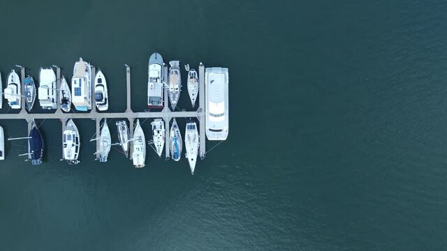 A moving drone view looking down at multiple boats docked on a wharf in a protected harbor located in the town of Bargara Bundargerg Queensland Australia