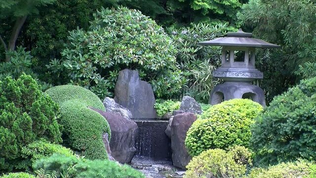 A stone lantern stands next to a waterfall in a Japanese garden.