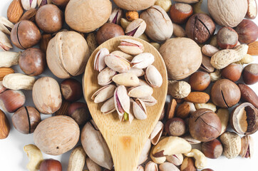 Pistachio nuts in a wooden spoon on the background of a scattering of different nuts assorted nuts