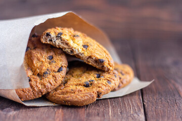 Delicious oatmeal cookies with chocolate pieces in wrapping paper on a wooden background.