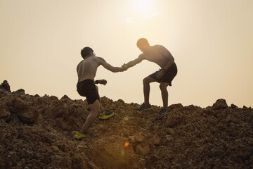 People helping each other hike up a mountain at sunrise. Giving a helping hand, and active fit lifestyle concept. Young asian couple climbing up on the mountain,hiking and team work concept. - obrazy, fototapety, plakaty