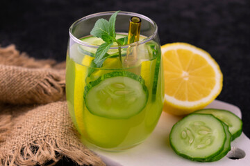 A glass of refreshing drink with cucumber, lemon and mint on a black background.
Close-up.