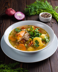 Shurpa - meat soup in a white plate on a wooden table. Restaurant, menu, recipe. Close-up, front view 