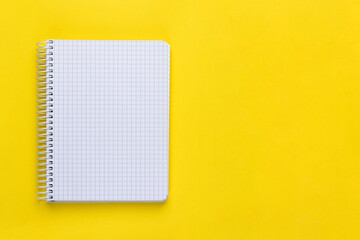Open spiral squared notebook or notepad with blank empty white sheets and binder on bright yellow background, top view, flat lay with copy space