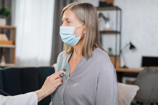 Pleasant Elderly Gray Haired Woman Having A Medical Examination At Home. Hand Of Female Doctor With Stethoscope Auscultating Senior Woman At Home, Checking Heart Beat And Breath.