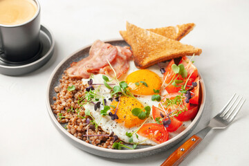 Healthy breakfast - eggs, toast, buckwheat, bacon, beans and tomatoes on a plate on the table.