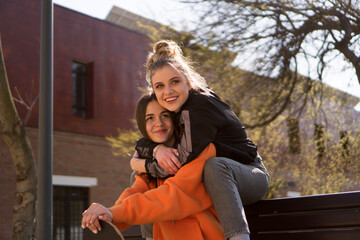 Two teenage skater girls are hanging out in the neighborhood, chatting and smiling.