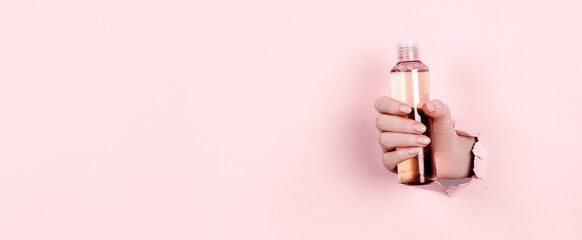 Female hands holding beauty bottles on abstract pink background. Horizontal view copyspace.