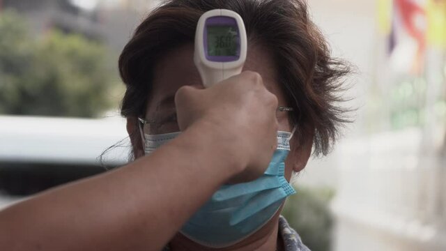 Covid -19 Body temperature measuring for coronavirus. Measures a senior Asian female’s temperature using a non-contact infrared thermometer.