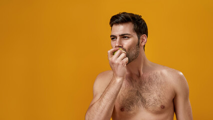 Fototapeta premium Young bearded man with naked torso eating apple