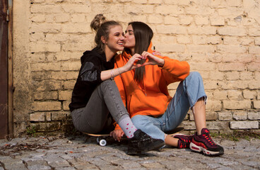 Two teenage skater girls are hanging out in the neighborhood, chatting and smiling.