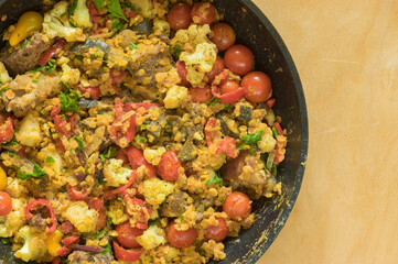 Top view on frying pan full of red lentils coocked with vegetables - red tomotoes,  mangold , parsley, cauliflower, egg-plant,   standing on a wooden surface