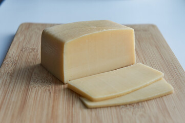 Two slices of cheese and square big piece of cheese on a wooden cutting board