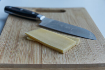 Two slices of cheese with a n iron knife  on a wooden cutting board
