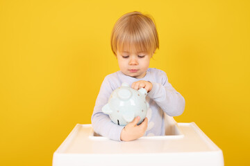 Beautiful smiling boy sitting with piggy bank isolated over yellow background.