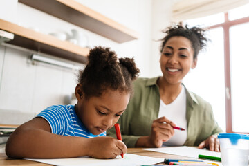 Naklejka premium Black smiling woman drawing with her daughter at home kitchen