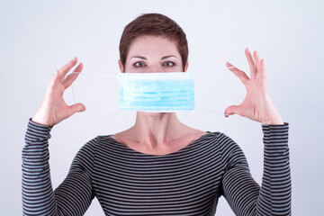 Beautiful woman with short hair removing her face mask in a bold gesture. Life in quarantine. Dealing with coronavirus restrictions. Life during pandemic. Quarantine ending.