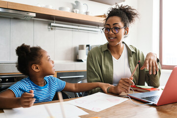 Naklejka premium Black woman working with laptop while sitting at table with her daughter