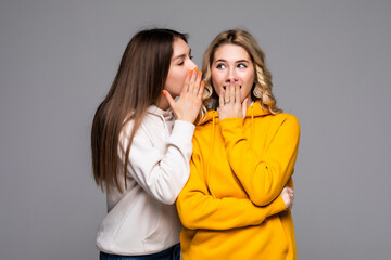 Young woman telling gossip to her girlfriend isolated over gray background