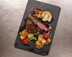 Juicy Beef rump steak from marble beef medium rare with spices and grilled vegetables on black stone plate, close-up.