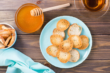 Small baguette toast on a plate on a wooden table. Homemade tea with honey. Top view