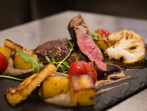 Juicy Beef rump steak from marble beef medium rare with spices and grilled vegetables on black stone plate, close-up.