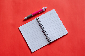 Opened notepad and pink pen on a red background.