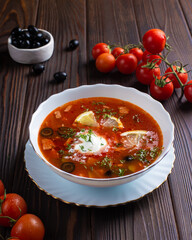 Borscht with lemon and olives in a white plate on a wooden table. Restaurant, menu, recipe. Close-up, front view 
