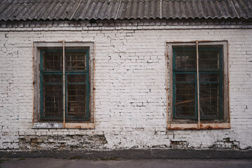 White brick wall of an old building. Two windows closed with bars.