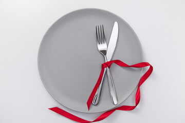 Festive table setting with red ribbon. Fork and knife on a gray plate and card postcard for text. Copy space. High quality photo