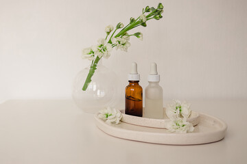 Two glass bottles for cosmetic, natural medicine , essential oil in the  ceramic plates decorated with flowers and a round vase on a white background. Eco safe beauty product concept.