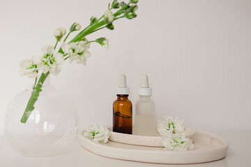 Two glass bottles for cosmetic, natural medicine , essential oil in the  ceramic plates decorated with flowers and a round vase on a white background. Eco safe beauty product concept.