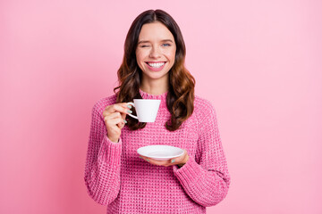 Portrait of attractive cheerful wavy-haired girl drinking beverage winking isolated over pink pastel color background