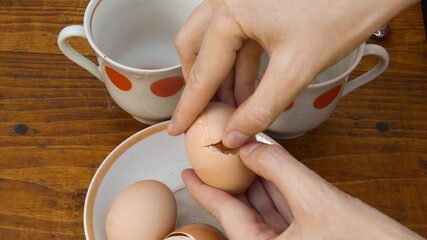 Fingers try to open eggshell of organic raw egg. Preparation of chicken eggs for cooking ang baking. Rustic kitchen crockery on background