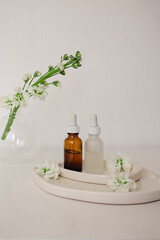 Obraz na płótnie Canvas Two glass bottles for cosmetic, natural medicine , essential oil in the ceramic plates decorated with flowers and a round vase on a white background. Eco safe beauty product concept.