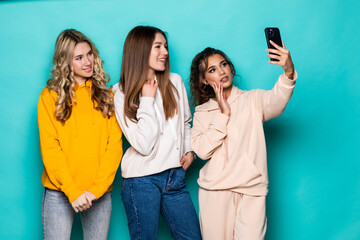 Young three multiethnic girlsfriends take a selfie by camera posing isolated over turquoise background