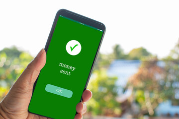 A man's hand holds a smartphone on the screen with the message money sent. Concept of financial...