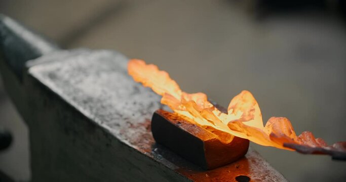 Blacksmith forges the red hot decorative metal product with hammer on the anvil, decorative forging of the metal flower, 4k Prores HQ