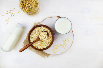 Oatmeal milk in a glass and a bottle, oatmeal flakes in a ceramic bowl on a white wooden background. Vegetable milk. Vegan lactose free. Top view