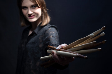 portrait of a cheerful rock n roll drumming girl holding sticks in her hands. Musician in black. On a dark background