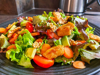 Plate with fresh salad made from lettuce, tomatoes, carrots, walnuts and vegan poultry.