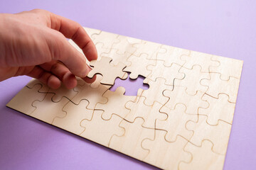 hand holding a jigsaw piece and complete puzzle on the table