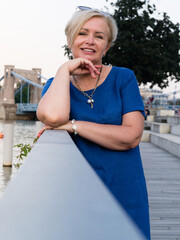 Happy elderly blonde woman in blue dress in summer park.