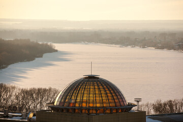 Obraz premium a bright orange sunset lights up buildings, an industrial area, and a river covered in snow