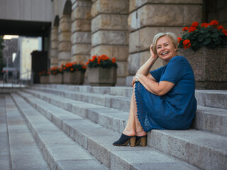 Happy elderly blonde woman in blue dress in summer park.