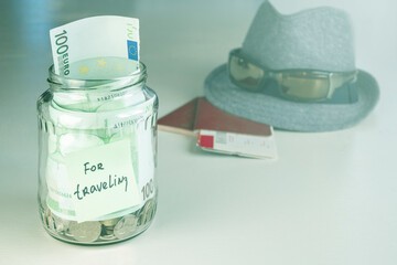 The glass jar with the words For travel on it is filled with coins and banknotes. A concept savings, piggy bank, money-saving travel jar. Copy space. Space for text.