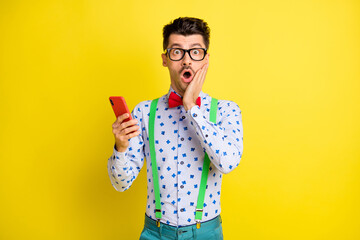Photo of young man amazed shocked surprised use cellphone dislike comment news isolated over yellow...